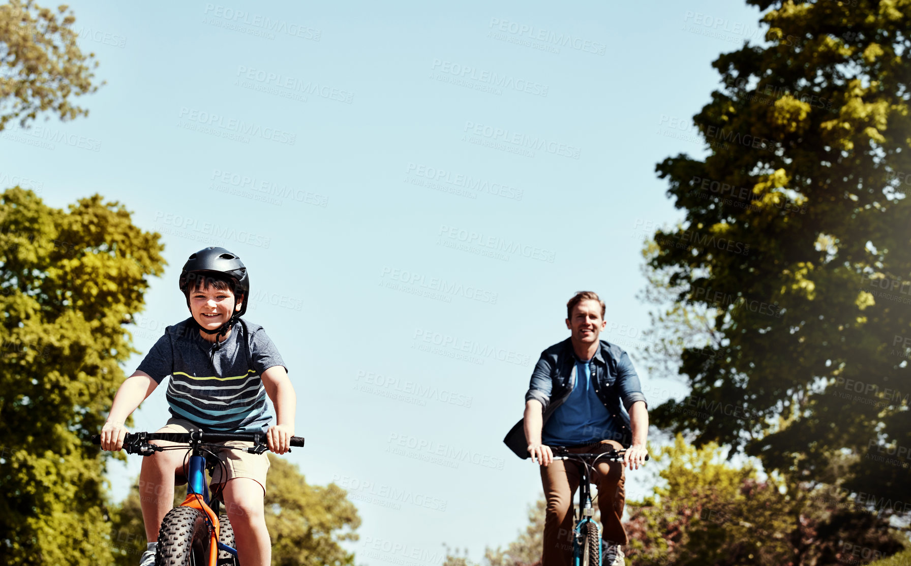 Buy stock photo Shot of a young boy and his father riding together on their bicycles