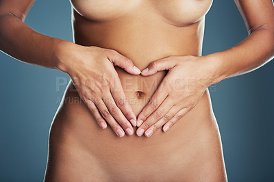 Buy stock photo Studio shot of an unrecognizable woman making a heart shape on her tummy while posing nude against a grey background