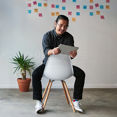 Buy stock photo Full length shot of a handsome young businessman sitting on a chair and using his digital tablet at work