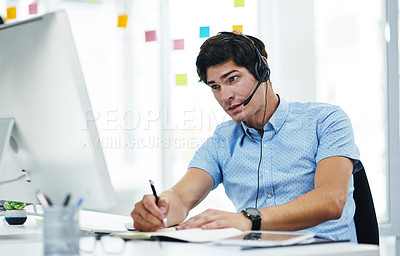Buy stock photo Shot of a young businessman using a headset while working on a computer in an office