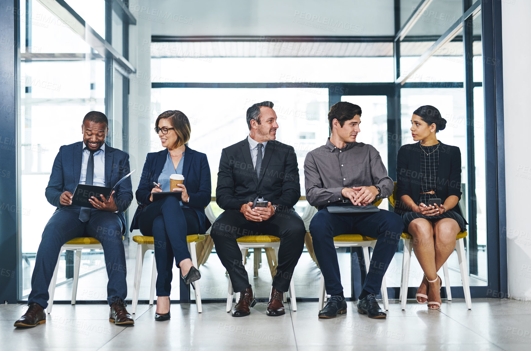 Buy stock photo Full length shot of a diverse group of businesspeople conversing with each other while sitting in line for an interview in a modern office