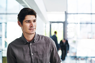 Buy stock photo Cropped shot of a handsome young businessman looking thoughtful in a modern office with his colleagues in the background