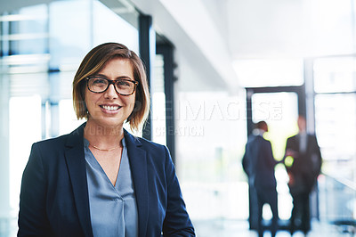 Buy stock photo Cropped portrait of an attractive young businesswoman smiling while standing in an office with her colleagues in the background