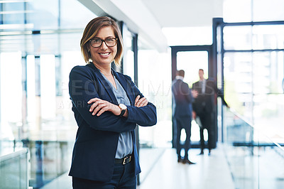 Buy stock photo Cropped portrait of an attractive young businesswoman standing with her arms folded in an office with her colleagues in the background