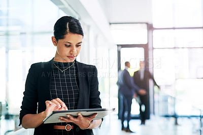Buy stock photo Cropped shot of an attractive young businesswoman using a digital tablet in an office with her colleagues in the background
