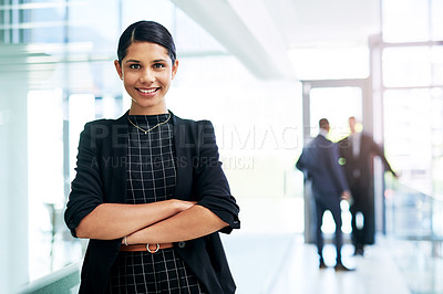 Buy stock photo Cropped portrait of an attractive young businesswoman standing with her arms folded in an office with her colleagues in the background