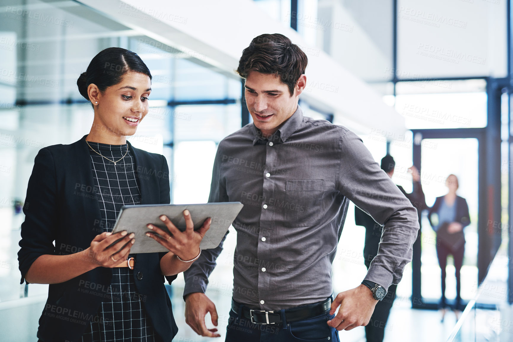 Buy stock photo Cropped shot of two young businesspeople a digital tablet while standing together in a modern office