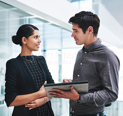 Buy stock photo Cropped shot of two young businesspeople a digital tablet while standing together in a modern office