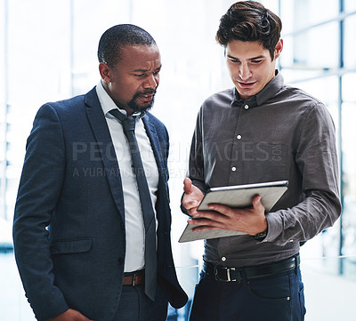 Buy stock photo Cropped shot of two young businessmen using a digital tablet together while standing in a modern office