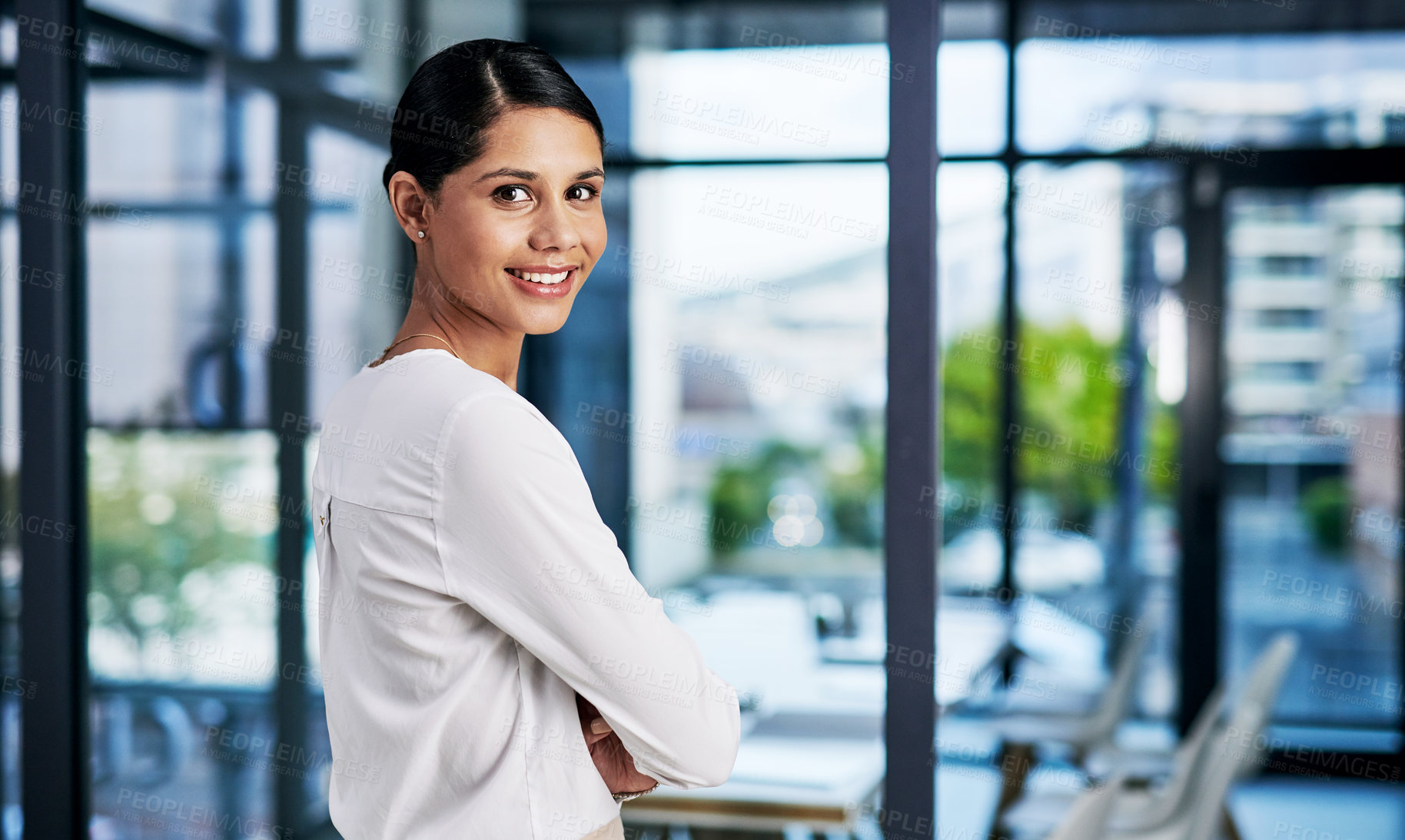 Buy stock photo Cropped portrait of an attractive young businesswoman smiling while standing with her arms folded in a modern office
