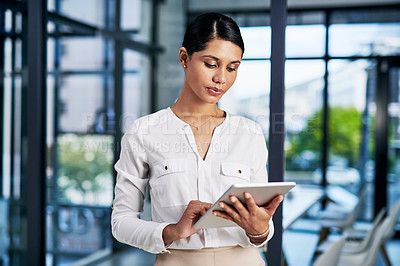 Buy stock photo Cropped shot of an attractive young businesswoman using a digital tablet while standing  in a modern office