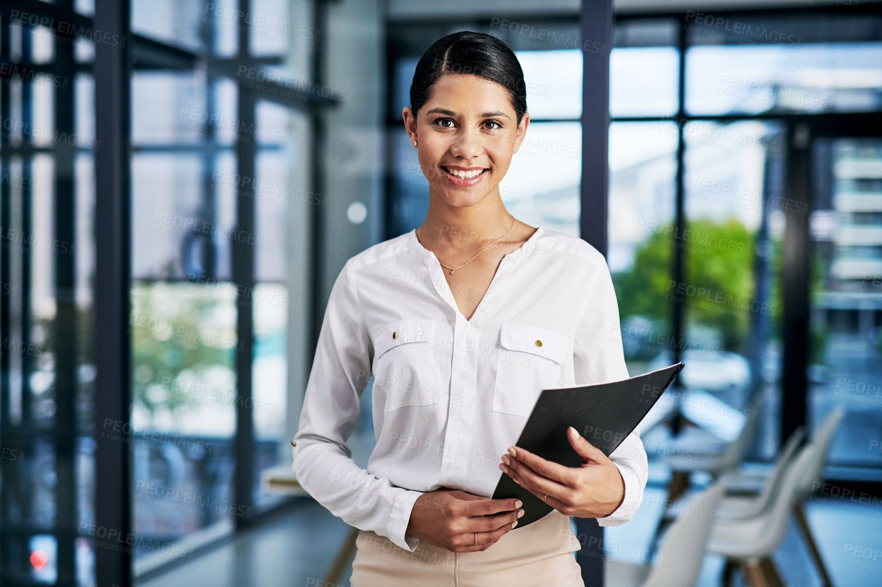 Buy stock photo Cropped portrait of an attractive young businesswoman smiling while holding a file in a modern office