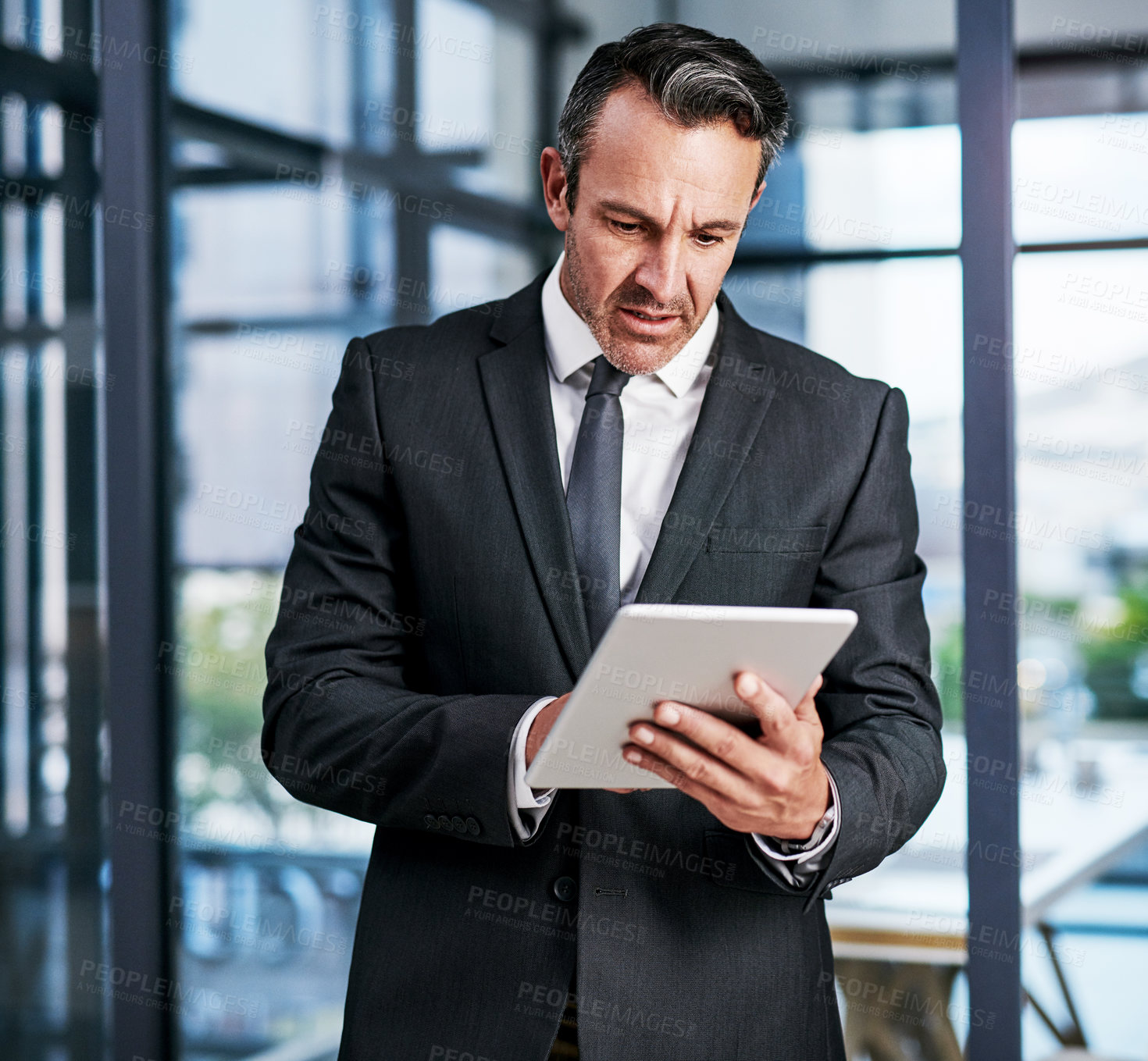 Buy stock photo Cropped shot of a handsome mature businessman using a digital tablet while standing in a modern office