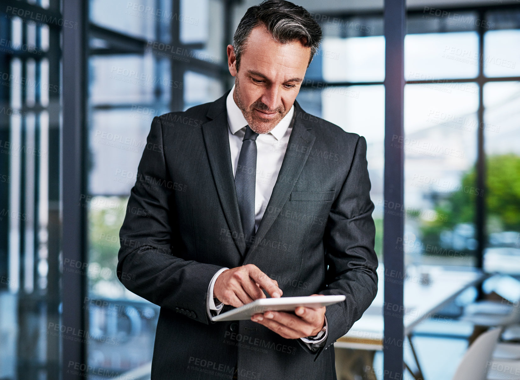 Buy stock photo Cropped shot of a handsome mature businessman using a digital tablet while standing in a modern office
