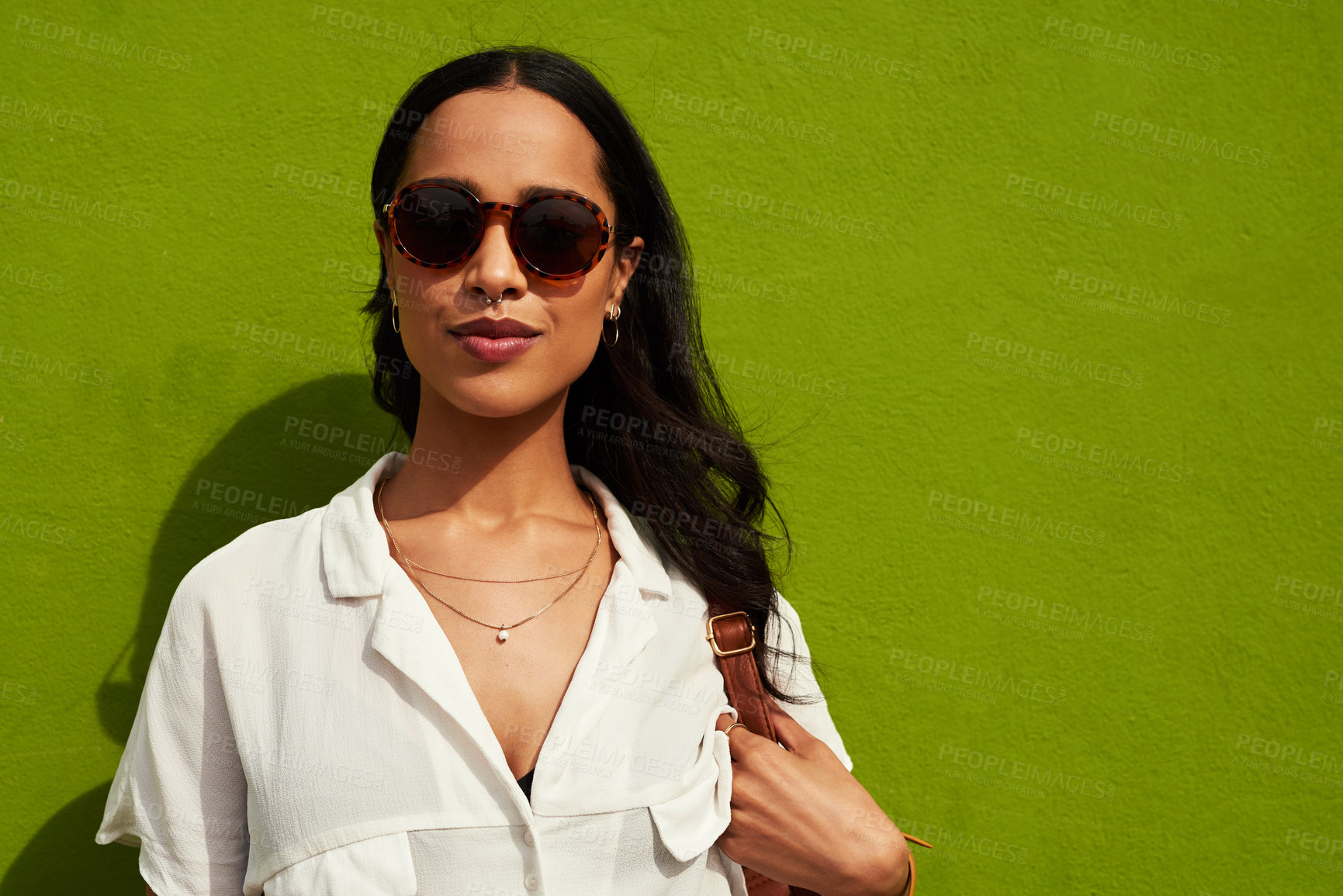 Buy stock photo Cropped portrait of an attractive young woman wearing sunglasses while standing alone against a green background in the city