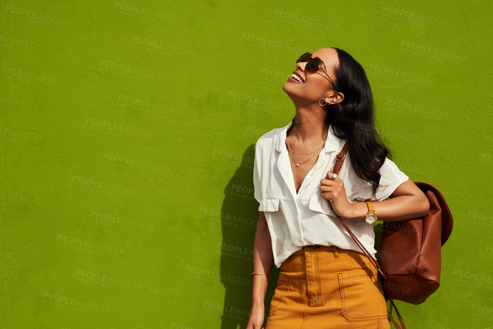 Buy stock photo Cropped shot of an attractive young woman wearing sunglasses while standing alone against a green background in the city