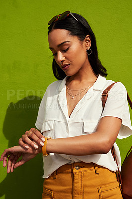 Buy stock photo Cropped shot of an attractive young woman looking at her watch while standing against a green background in the city