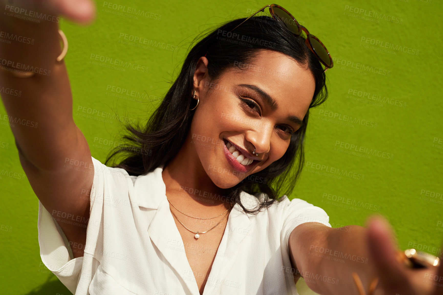 Buy stock photo Cropped portrait of an attractive young woman standing alone and taking a selfie against a green background in the city