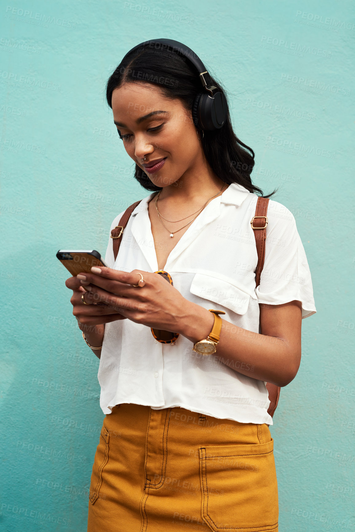 Buy stock photo Cropped shot of an attractive young woman standing alone and listening to music while texting against a blue background