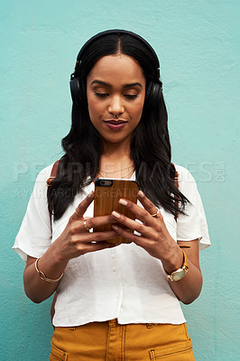Buy stock photo Cropped shot of an attractive young woman standing alone and listening to music while texting against a blue background