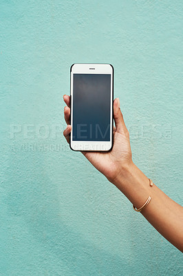 Buy stock photo Cropped shot of an unrecognizable woman holding her cellphone against a blue background in the city