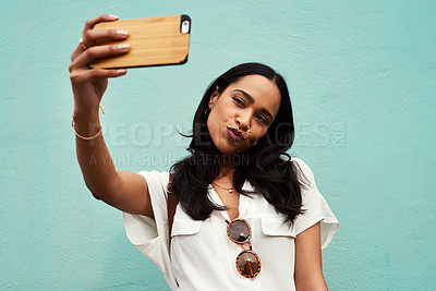 Buy stock photo Cropped shot of an attractive young woman standing and using her cellphone to take a selfie against a blue background