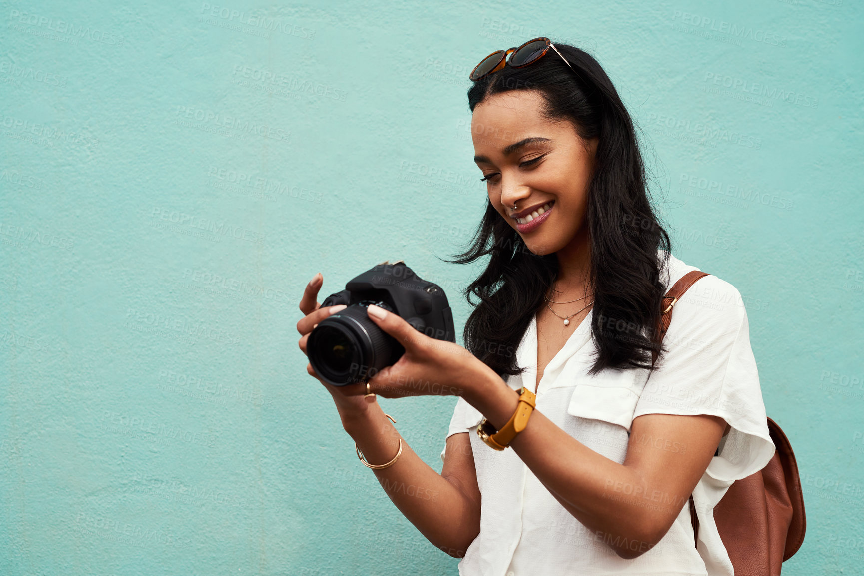 Buy stock photo Cropped shot of an attractive young woman standing alone against a blue background in the city and holding her camera