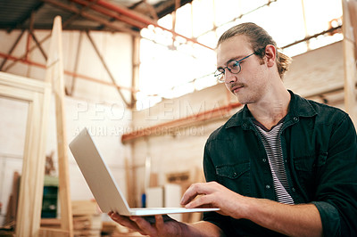 Buy stock photo Cropped shot of a handsome young carpenter using a laptop while working inside his workshop