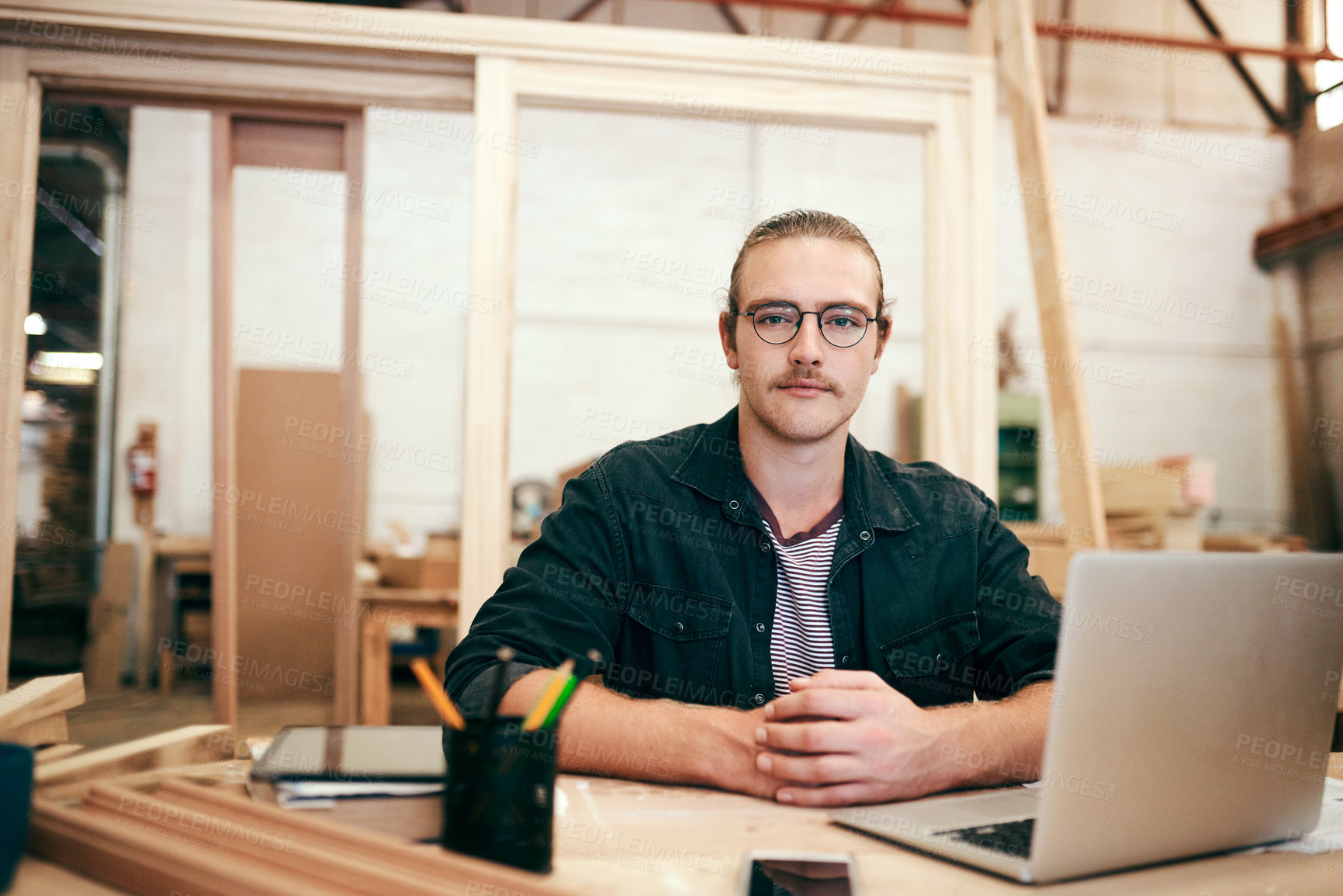 Buy stock photo Portrait of a handsome young carpenter working on a laptop inside his workshop