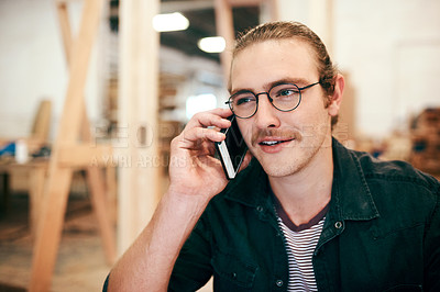 Buy stock photo Cropped shot of a young carpenter making a phone call while working inside his workshop