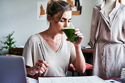 Buy stock photo Shot of a young designer drinking green juice while working at her desk