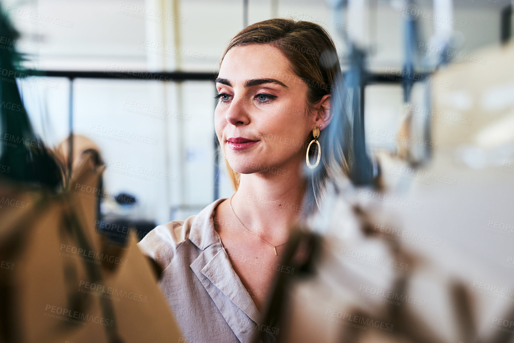 Buy stock photo Cropped shot of a designer looking at garments on a railing in her workshop