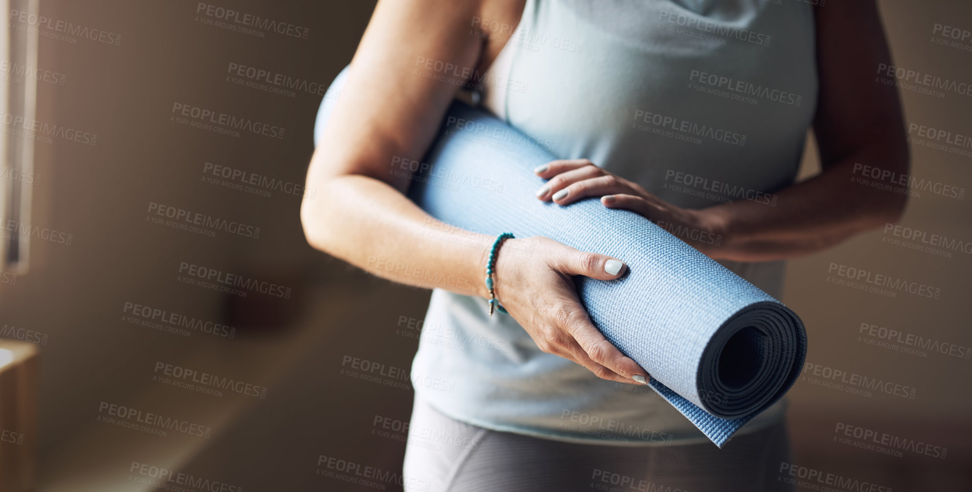 Buy stock photo Cropped shot of an unrecognizable woman standing alone and holding her yoga mat before an indoor yoga session