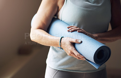 Buy stock photo Cropped shot of an unrecognizable woman standing alone and holding her yoga mat before an indoor yoga session