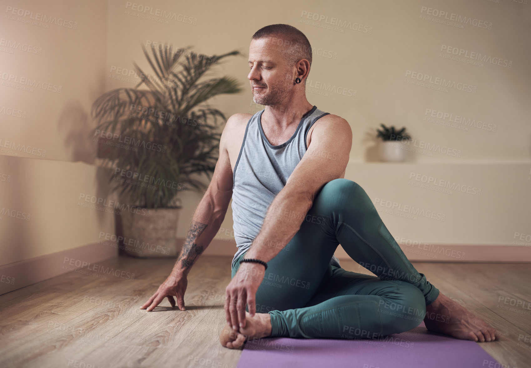 Buy stock photo Full length shot of a handsome young man sitting and holding a spinal half twist during an indoor yoga session