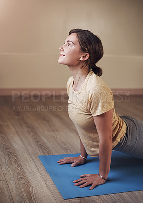 Buy stock photo Cropped shot of an attractive young woman holding an upward facing dog pose during an indoor yoga session alone