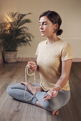 Buy stock photo Full length shot of an attractive young woman sitting indoors and using mala beads during her meditation routine
