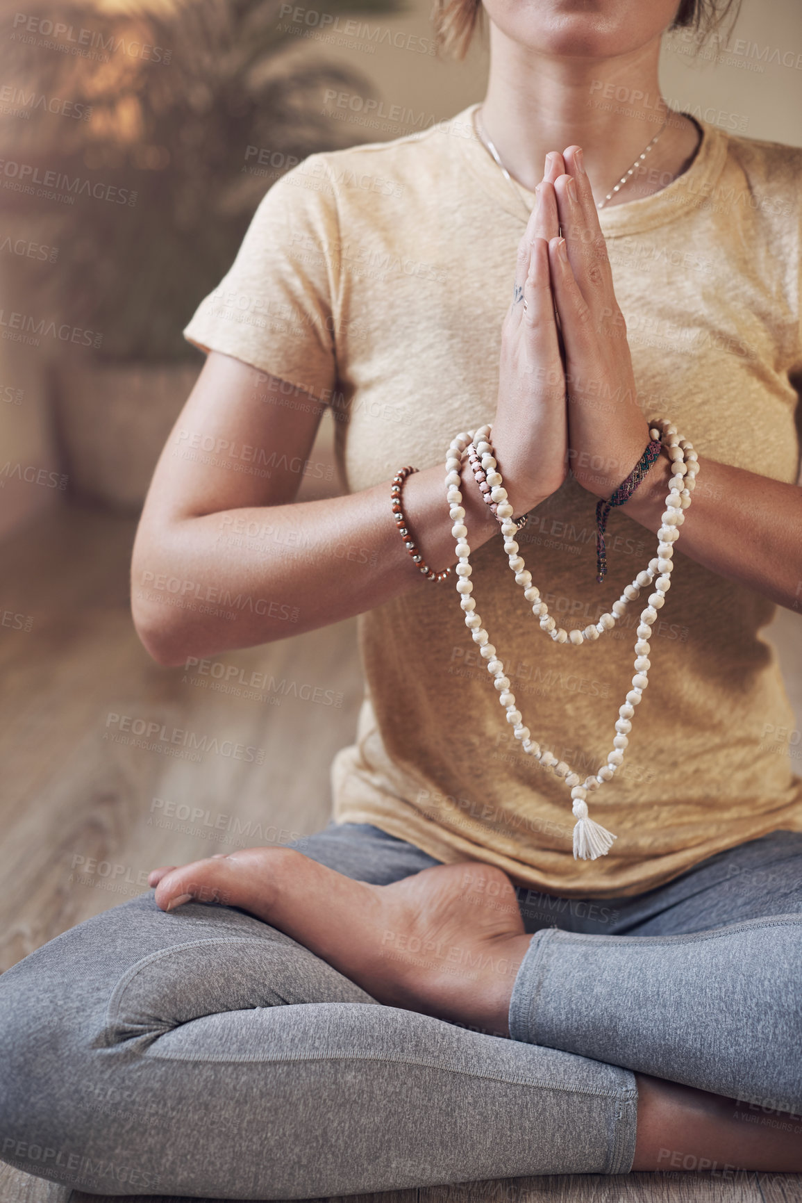 Buy stock photo Cropped shot of an unrecognizable woman sitting indoors and using mala beads during her meditation routine