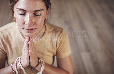 Buy stock photo Cropped shot of an attractive young woman sitting indoors and using mala beads during her meditation routine