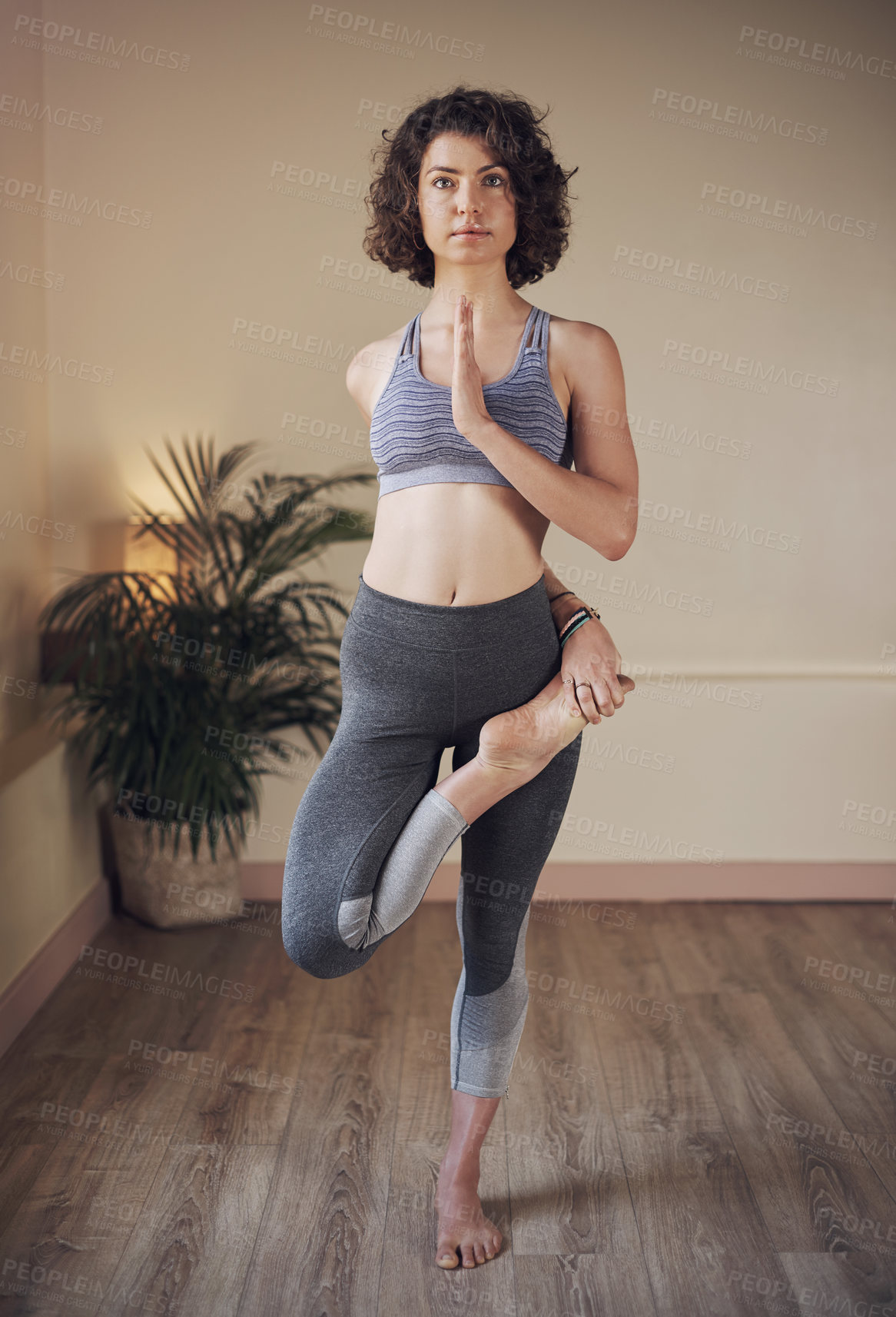 Buy stock photo Full length shot of an attractive young woman standing and holding an advanced yoga pose during an indoor yoga session