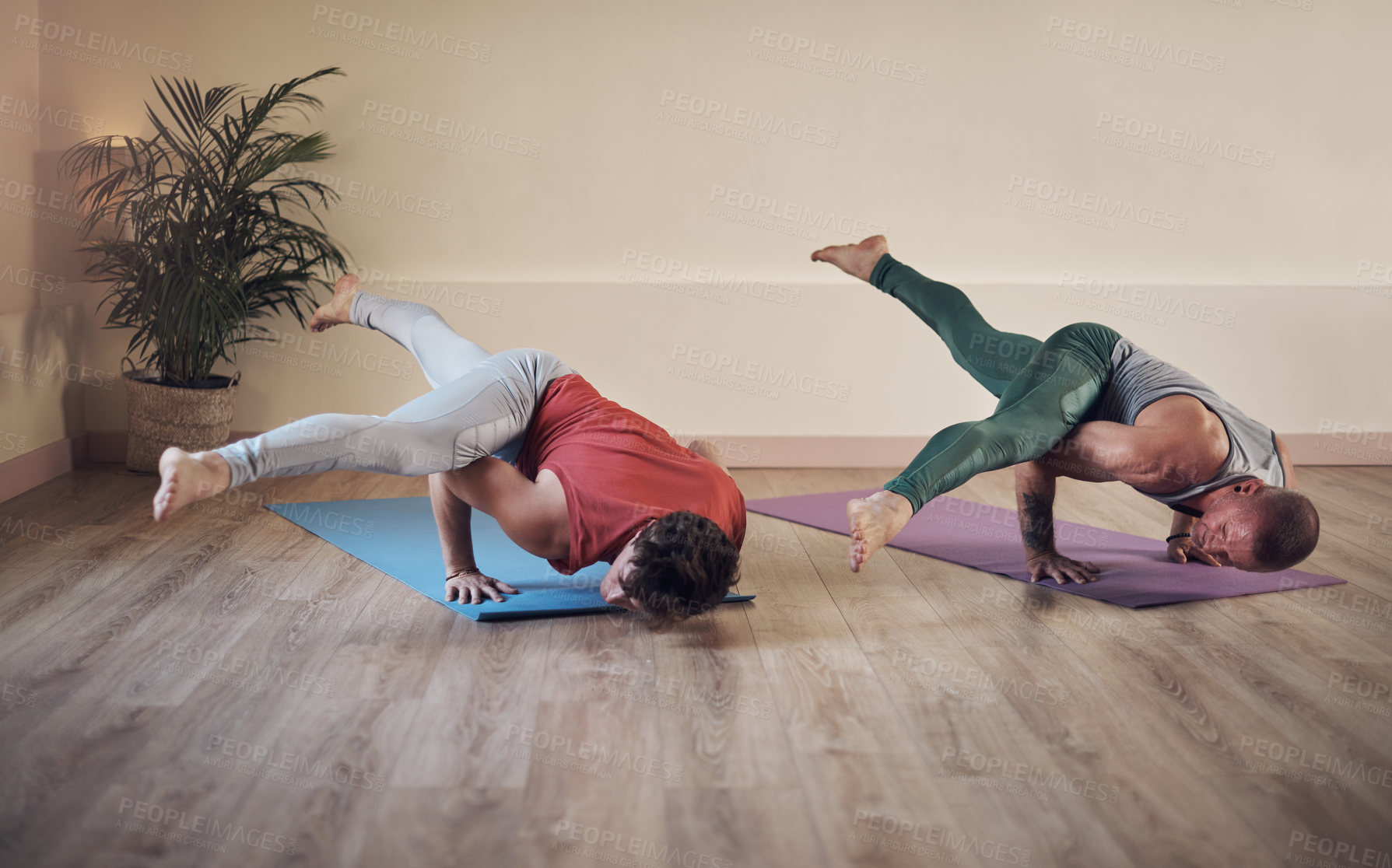 Buy stock photo Full length shot of two young men holding an extended side crow pose during an indoor yoga session together