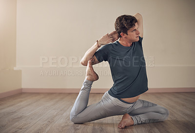 Buy stock photo Full length shot of a handsome young man holding a mermaid's pose during an indoor yoga session alone