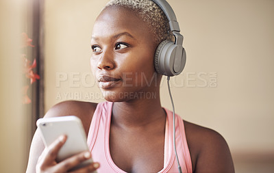 Buy stock photo Cropped shot of an attractive young woman sitting and wearing headphones while listening to music through her cellphone