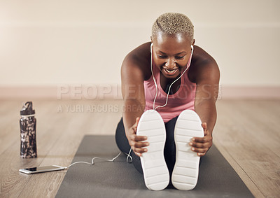 Buy stock photo Full length shot of an attractive young woman sitting alone and stretching before a workout indoors