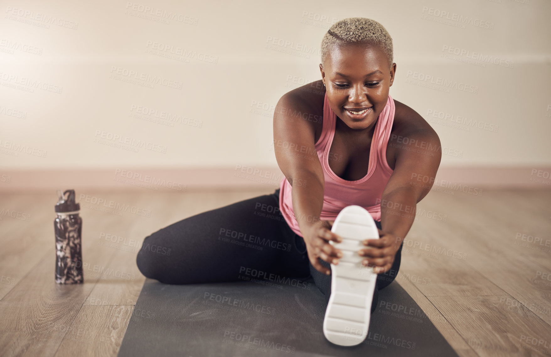 Buy stock photo Full length shot of an attractive young woman sitting alone and stretching before a workout indoors
