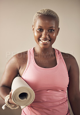 Buy stock photo Cropped portrait of an attractive young woman standing alone and holding her yoga mat before an indoor yoga session