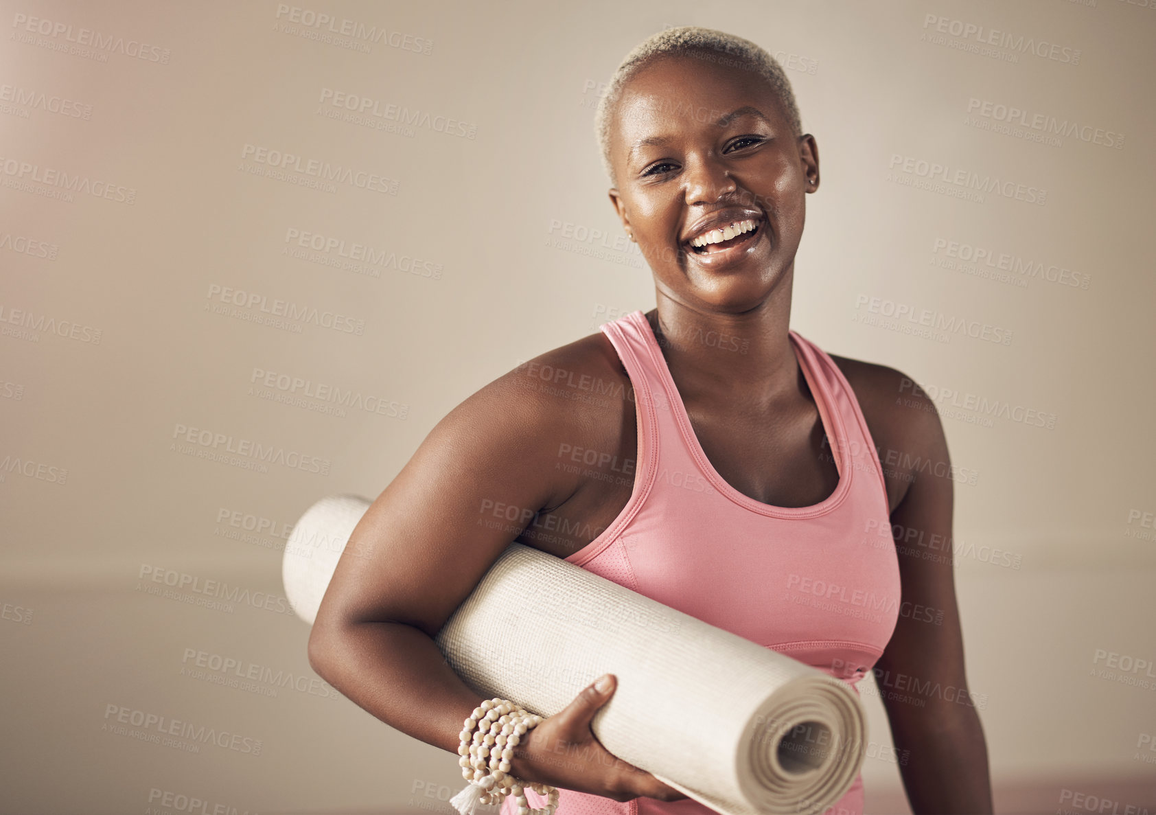 Buy stock photo Cropped portrait of an attractive young woman standing alone and holding her yoga mat before an indoor yoga session