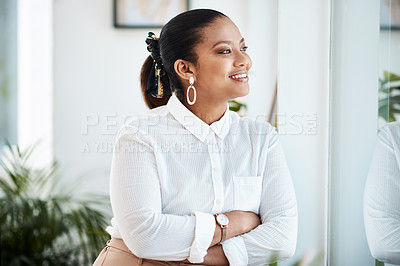 Buy stock photo Shot of a young businesswoman looking thoughtfully out of a window in a modern office