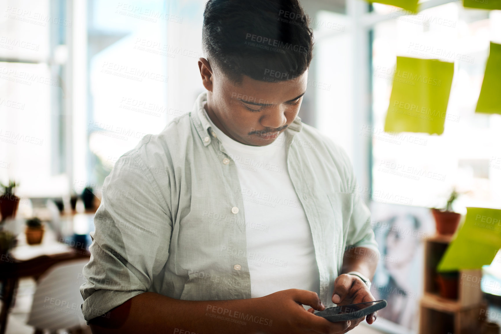 Buy stock photo Shot of a young businessman using a smartphone while having a brainstorming session in a modern office