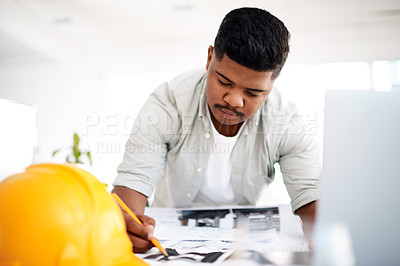 Buy stock photo Shot of a young businessman working on a blueprint in a modern office